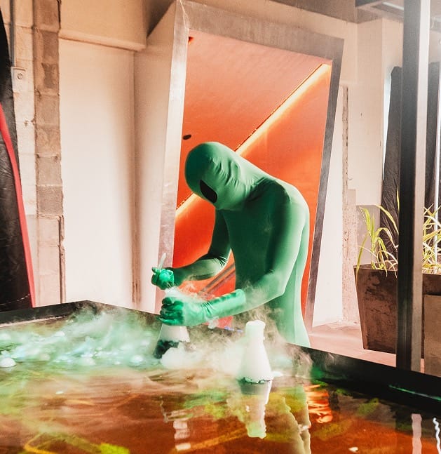 Performer de verde preparando un cóctel entre humo de hielo seco