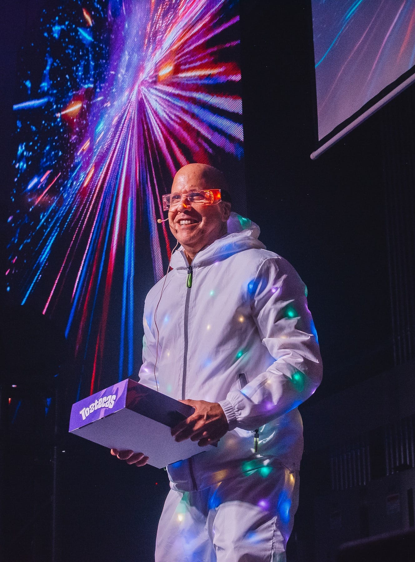 Presentador en escena con chaqueta luminosa ante una pantalla LED